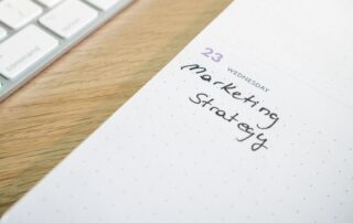 Close-up of a planner with 'Marketing Strategy' handwritten alongside keyboard.