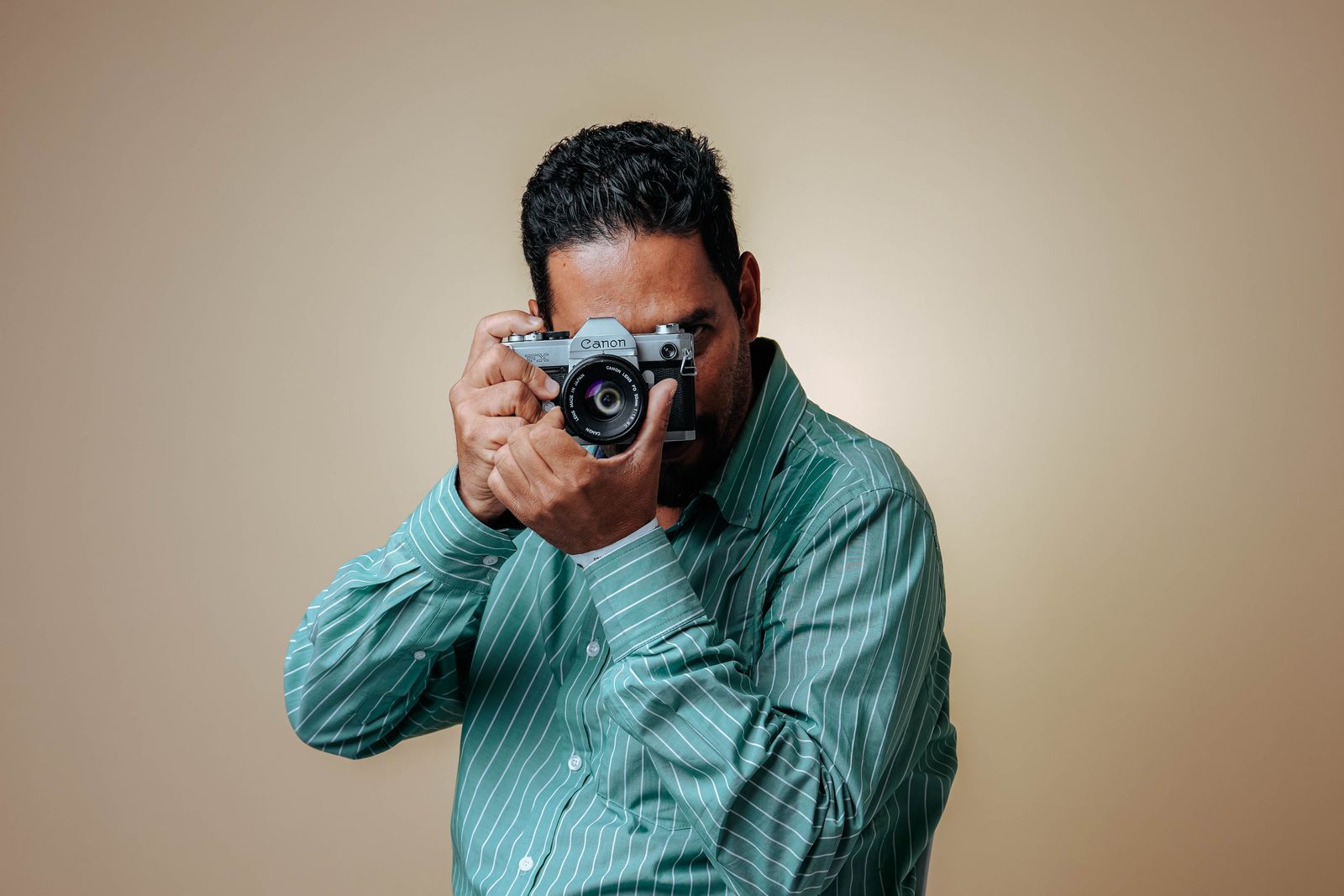 Man posing with a vintage camera in a studio setting wearing a striped green shirt.