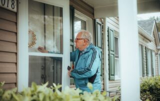 Elderly man in a blue jacket knocking on a suburban house door, showcasing community life.
