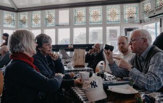 A group of senior adults enjoying conversation and coffee in a cozy café setting with stained glass windows.