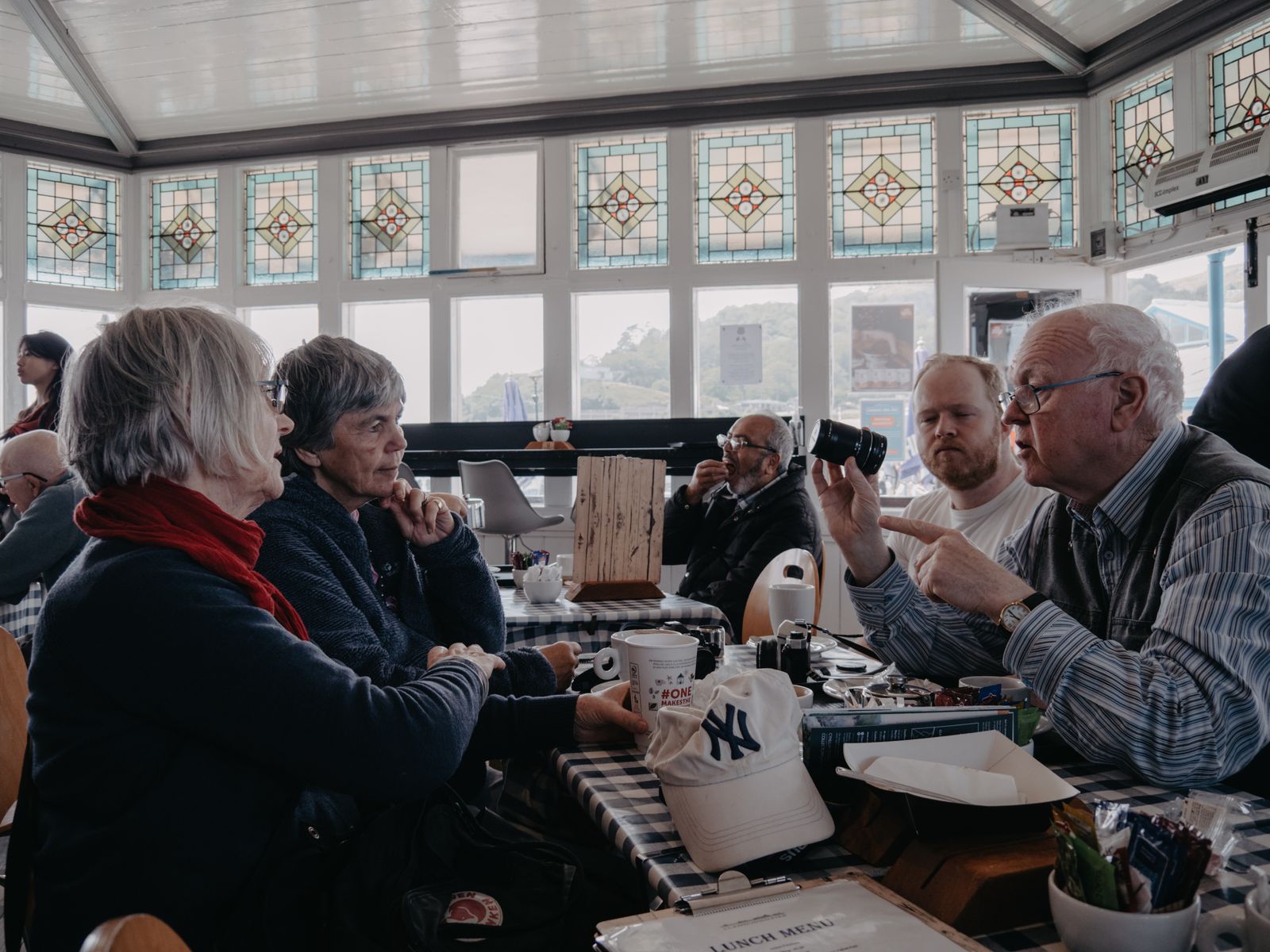 A group of senior adults enjoying conversation and coffee in a cozy café setting with stained glass windows.