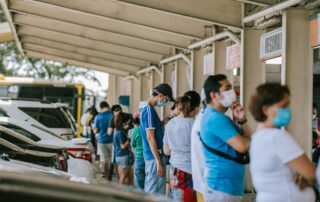 A group of people wearing face masks standing in line at an outdoor location.