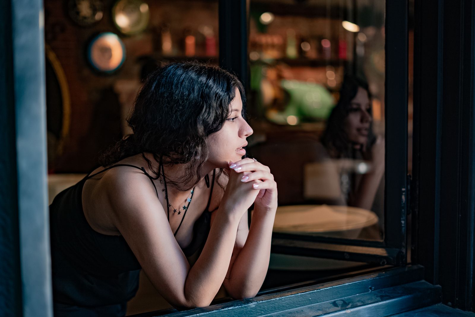 A thoughtful woman in a cozy cafe looks outside, reflecting on a peaceful day.
