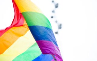 A colorful rainbow pride flag waves against a bright sky, symbolizing LGBTQ+ celebration and diversity.