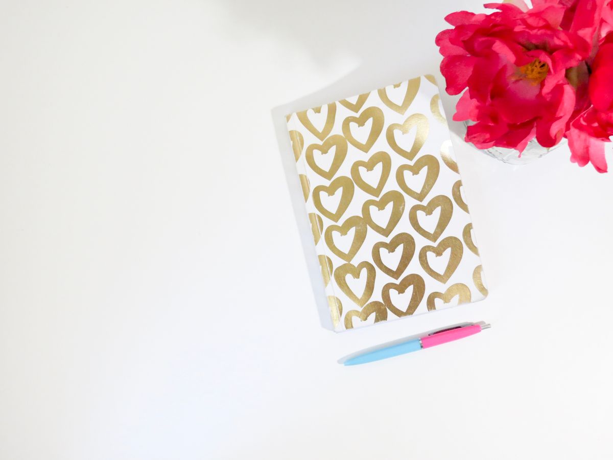 Notebook with gold hearts, a pen and pink flowers laid out on a desk