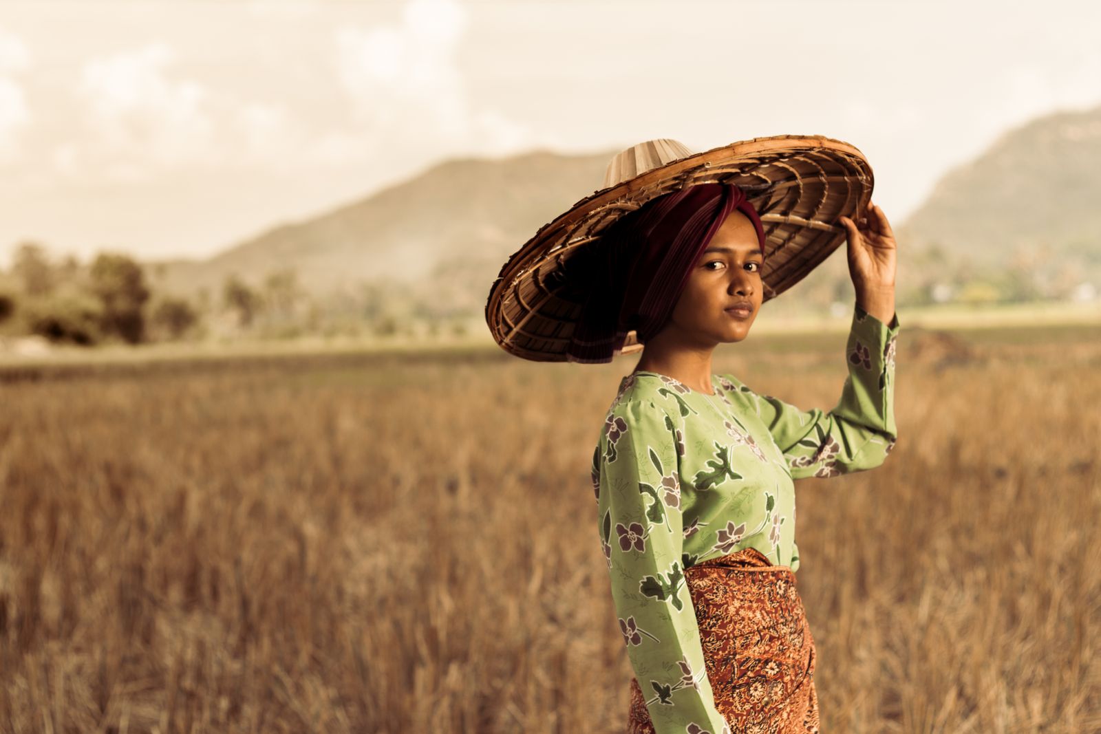Portrait of a woman in traditional dress with a straw hat in West Sumatra's rice fields.