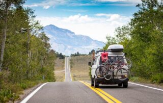 A camper van travels through a beautiful mountain landscape, bicycles mounted on the back.