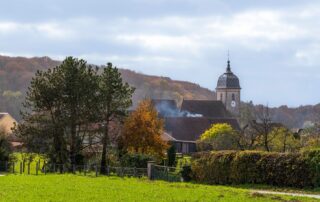 A picturesque French village landscape featuring a church tower and autumn foliage.