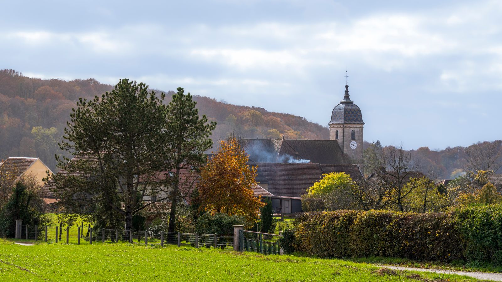 A picturesque French village landscape featuring a church tower and autumn foliage.