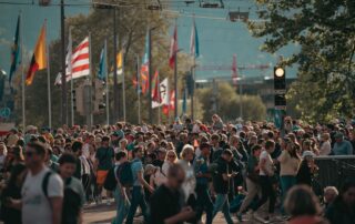 A bustling city street with a diverse crowd and international flags under a sunny sky.
