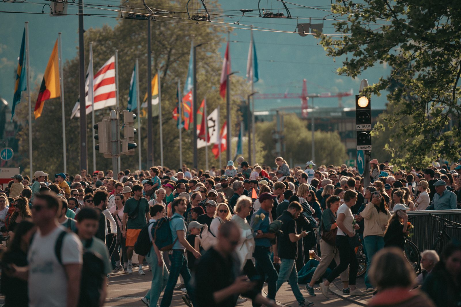 A bustling city street with a diverse crowd and international flags under a sunny sky.