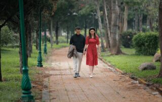 A couple walks hand in hand along a scenic park pathway surrounded by greenery.