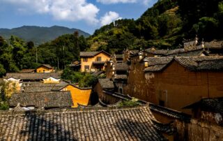 Explore the rustic charm and traditional architecture of an ancient Chinese village nestled in lush mountains.