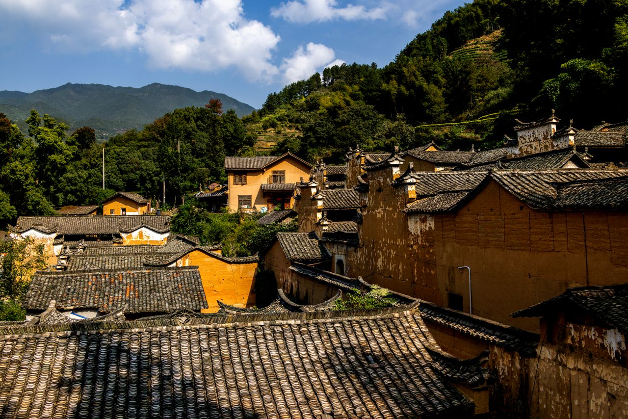 Explore the rustic charm and traditional architecture of an ancient Chinese village nestled in lush mountains.