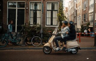 Blurred motion of a couple on a scooter passing a cozy European street with bicycles parked nearby.