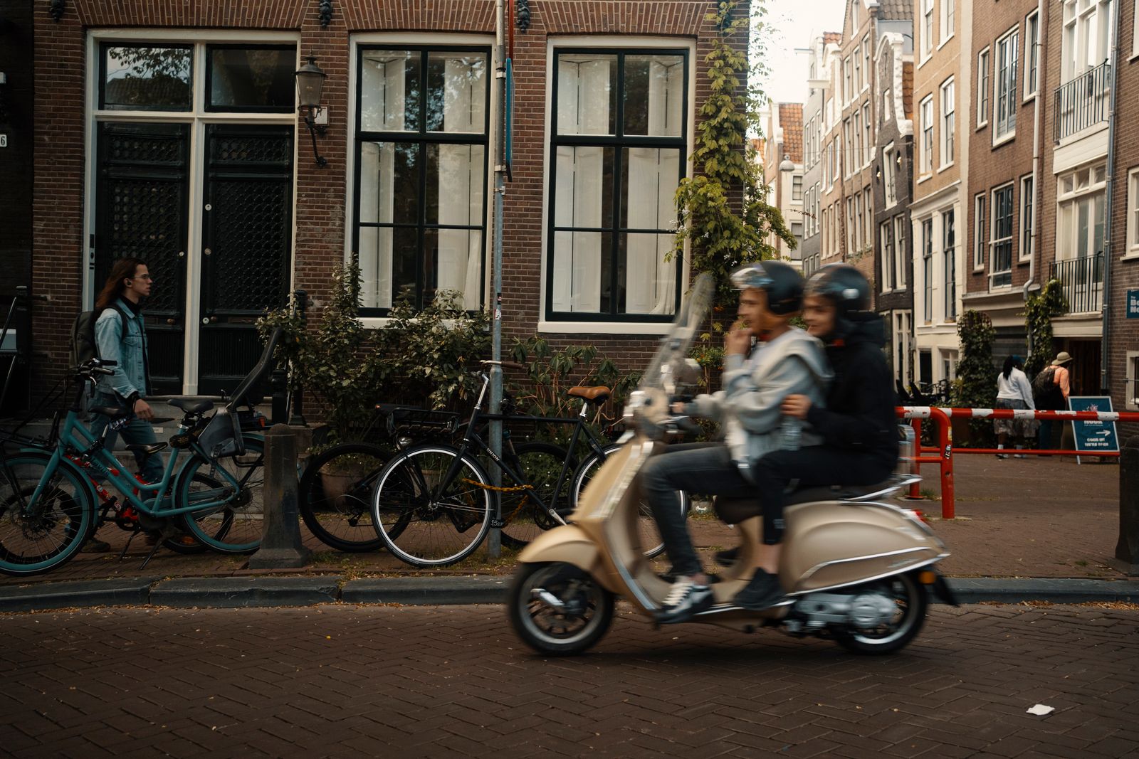 Blurred motion of a couple on a scooter passing a cozy European street with bicycles parked nearby.