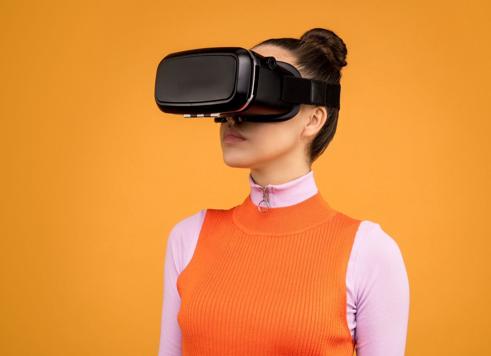Woman enjoying virtual reality with VR headset against vibrant orange background.