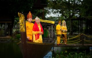 Couples in vibrant Indonesian wedding attire on a traditional wooden boat in Jakarta.