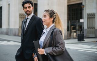 Two business professionals in formal attire walking on a city street, engaged in conversation.