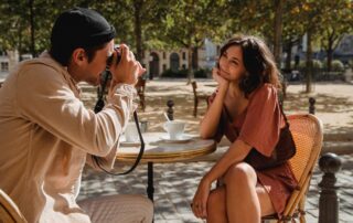 A couple enjoys a romantic moment in a sunlit outdoor cafe while taking photos.