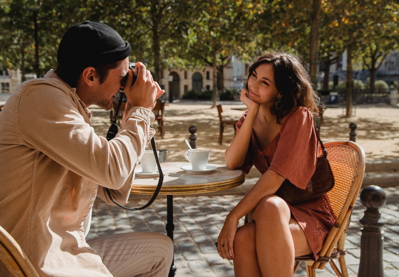 A couple enjoys a romantic moment in a sunlit outdoor cafe while taking photos.