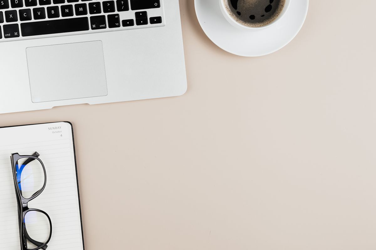 Office desk with a laptop, notebook, coffee and eyeglasses
