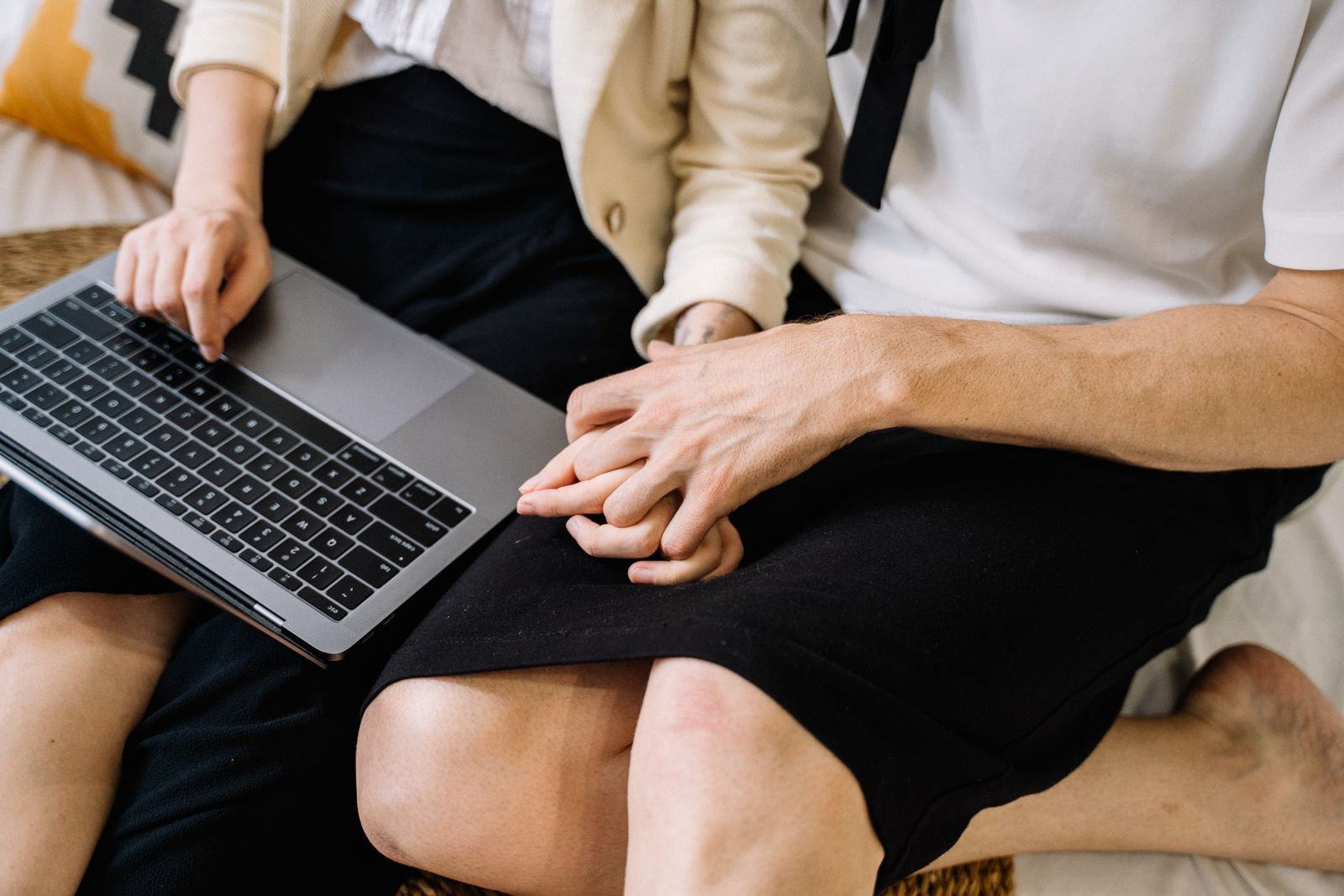 A close-up of a couple sitting together, using a laptop while holding hands.