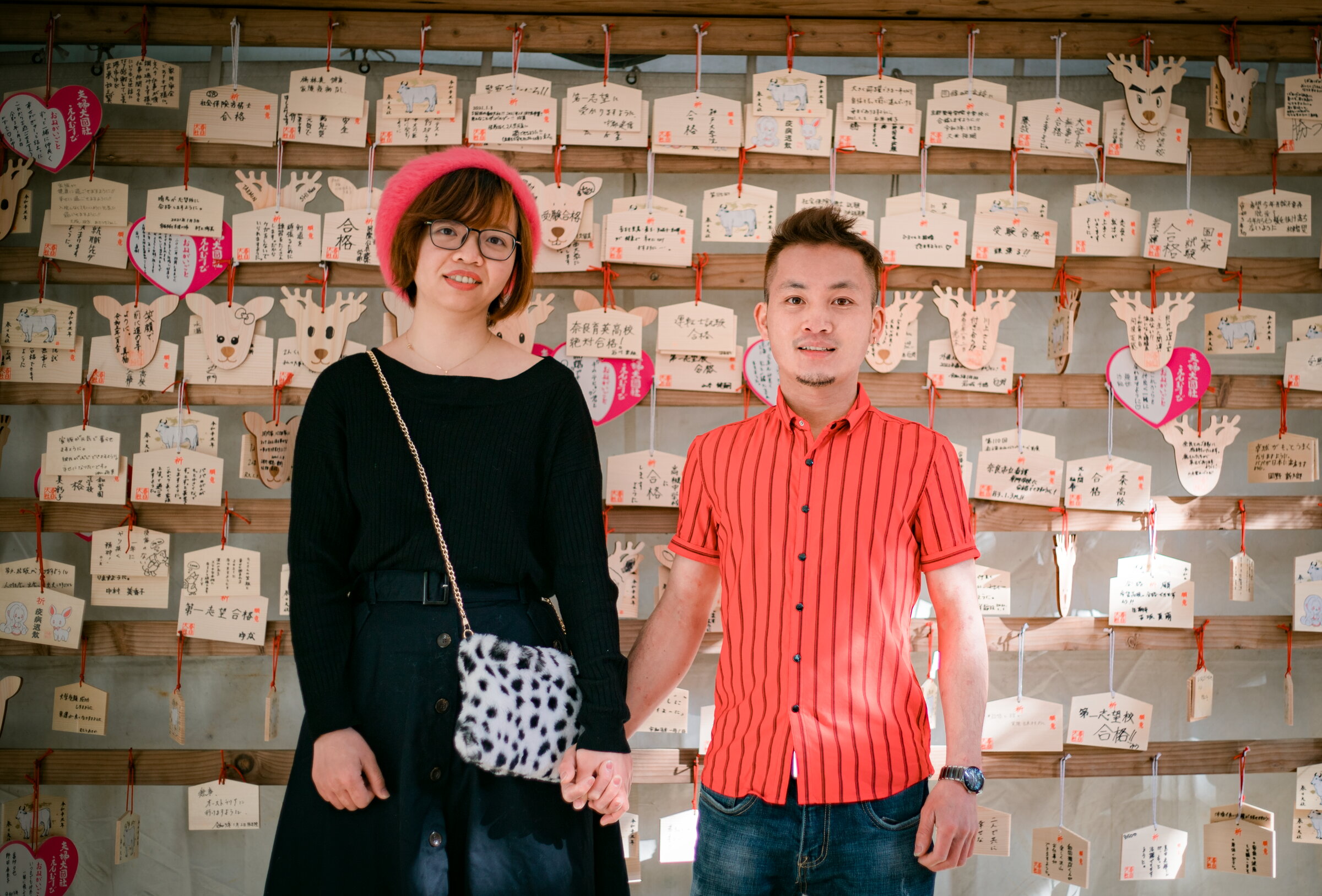 Couple holding hands in front of a wall of Japanese ema wish plaques