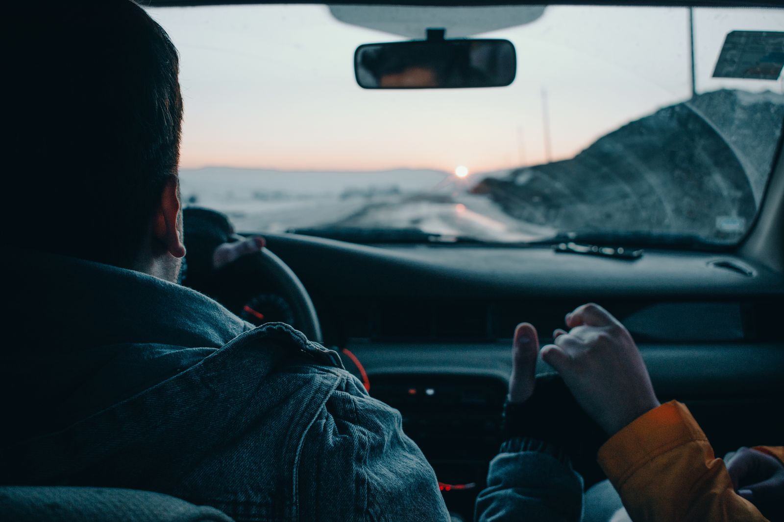 Back view of crop anonymous couple of travelers driving modern automobile along asphalt road at sunset