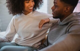 Crop positive African American female leaning on shoulder of black boyfriend while spending time together in light room