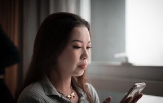 Young Asian woman using smartphone indoors, focused on screen.
