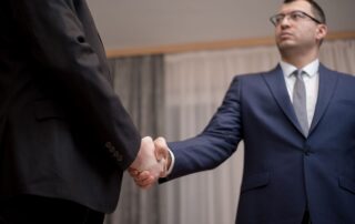 Two businessmen in formal attire shaking hands during a meeting.