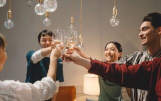 Group of young friends toasting with wine glasses, celebrating indoors under warm lighting.