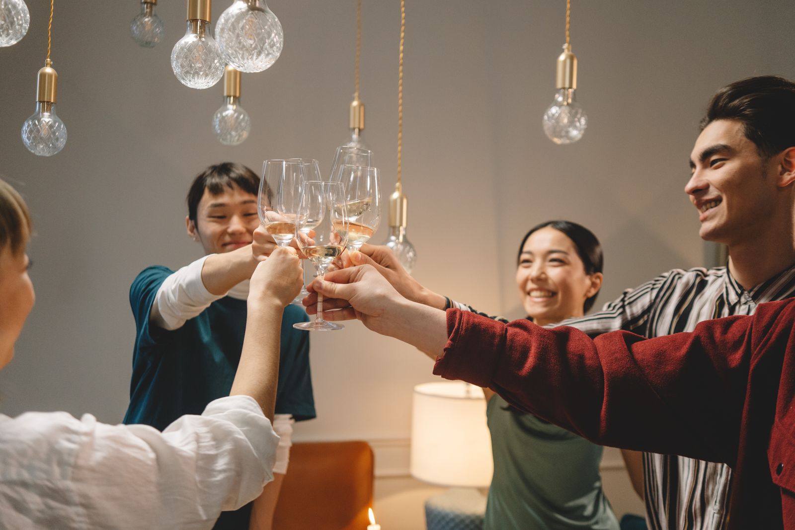 Group of young friends toasting with wine glasses, celebrating indoors under warm lighting.