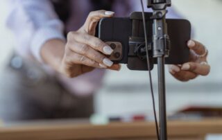 Crop unrecognizable female setting mobile phone on tripod while recording vlog on blurred background