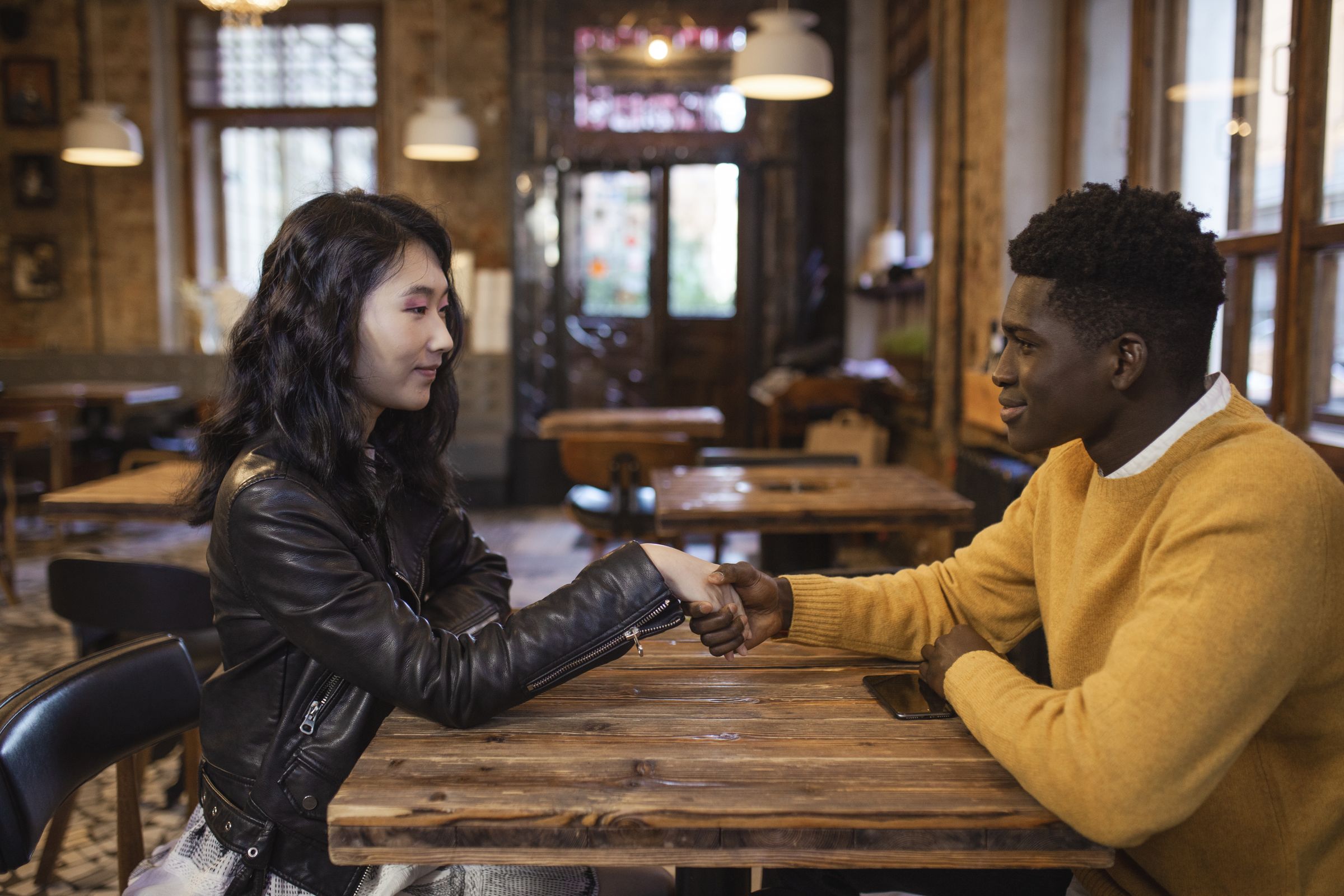 A man and a woman shaking hands as they meet across a cafe table