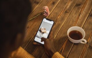 An individual using a dating app on a smartphone with a cup of tea nearby on a wooden table.