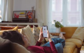 Woman relaxing and using a dating app on her smartphone while lying on a sofa indoors.
