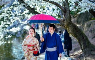 A couple in traditional kimonos walk under cherry blossoms holding an umbrella, symbolizing romance.
