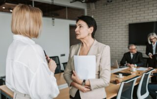 Two businesswomen engage in a conversation during a professional meeting in a modern office.
