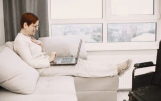 Mature woman enjoying a video call at home, smiling and relaxed on a sofa with a laptop.