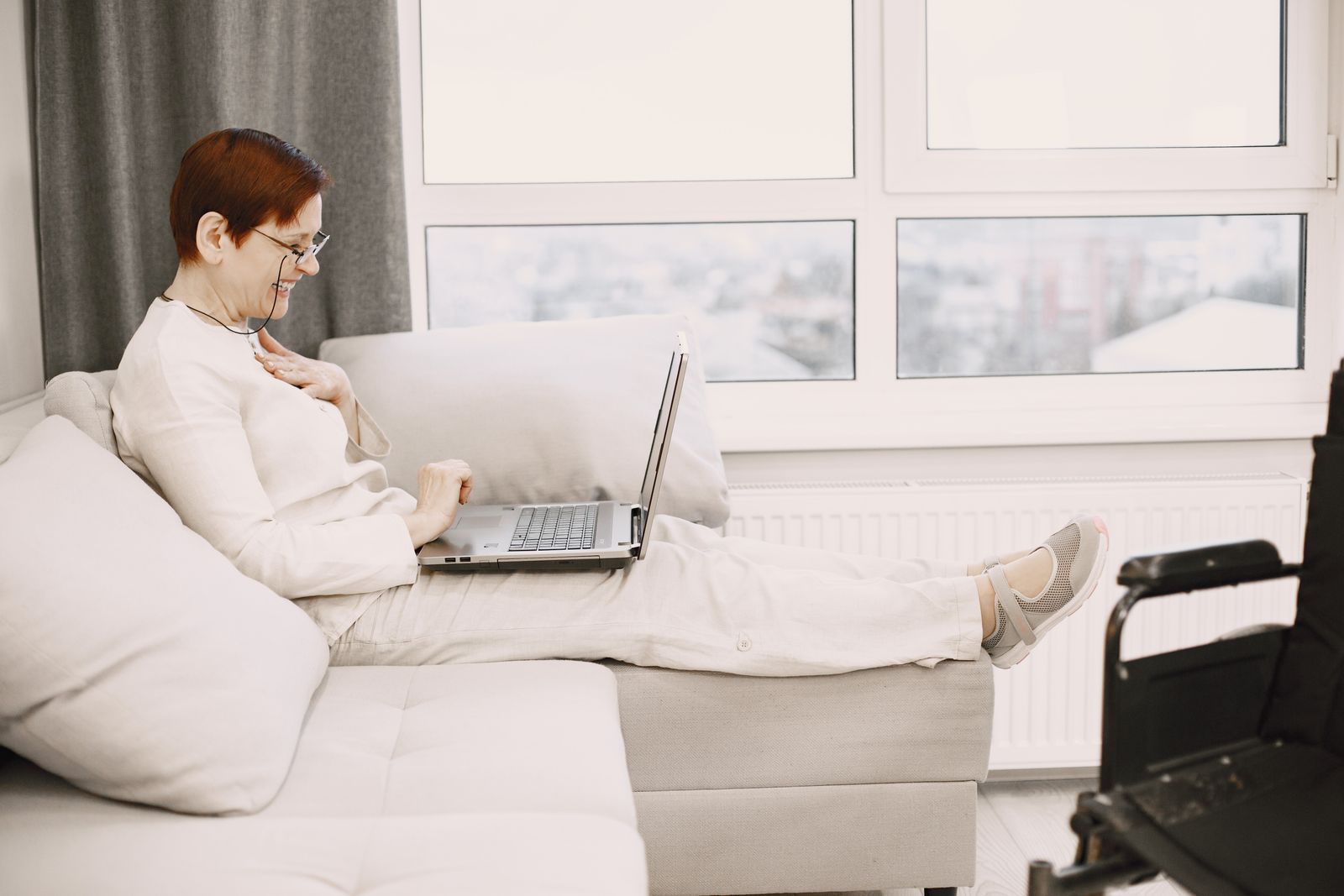 Mature woman enjoying a video call at home, smiling and relaxed on a sofa with a laptop.