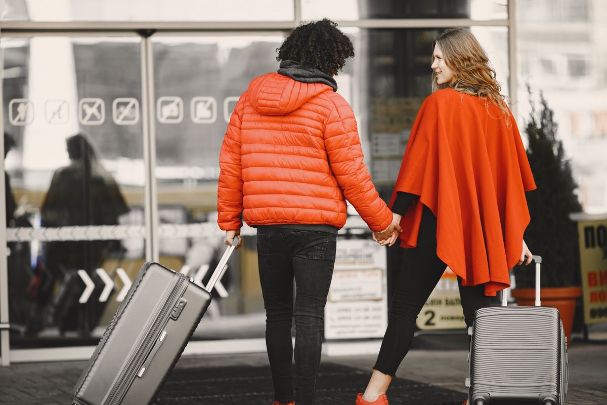 Couple holding hands with luggage entering an airport terminal
