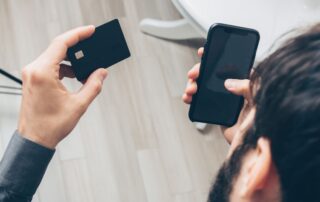 Close-up of man holding a smartphone and credit card, making an online payment indoors.