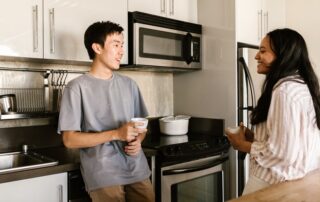 A man and a woman chatting happily while holding coffee cups in a modern kitchen.