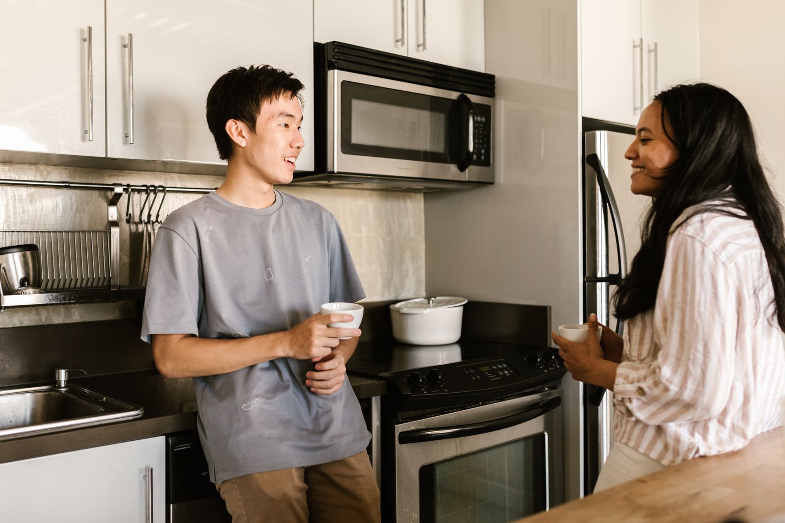 A man and a woman chatting happily while holding coffee cups in a modern kitchen.