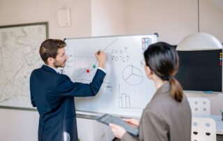 Two business professionals planning and discussing strategy at a whiteboard in a modern office setting.