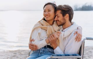 A happy couple embracing on a beach with a serene waterfront backdrop.