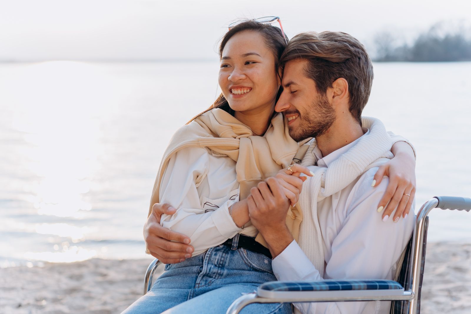A happy couple embracing on a beach with a serene waterfront backdrop.