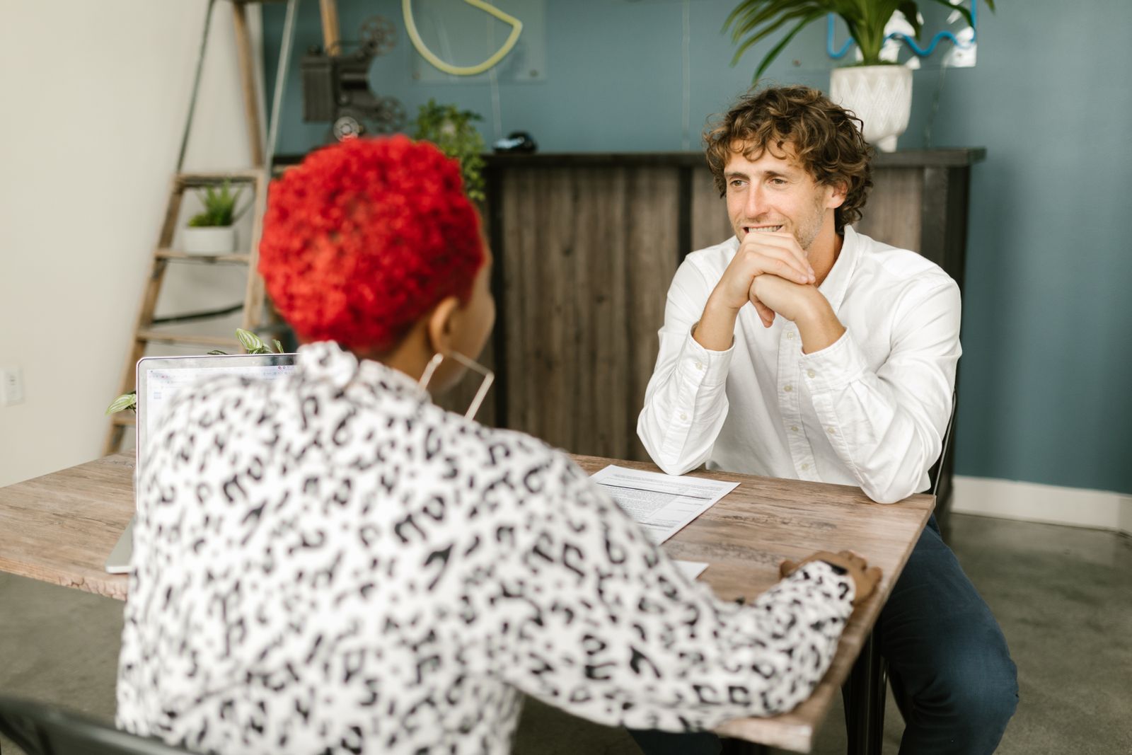Two adults engaging in a relaxed office conversation across a desk.